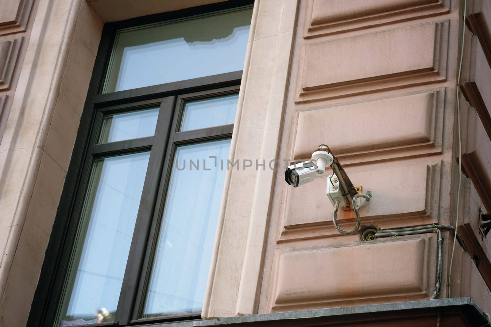 From a highangle perspective, a security camera is mounted on a building next to the window to ensure safety and continuous monitoring to avoid robbery