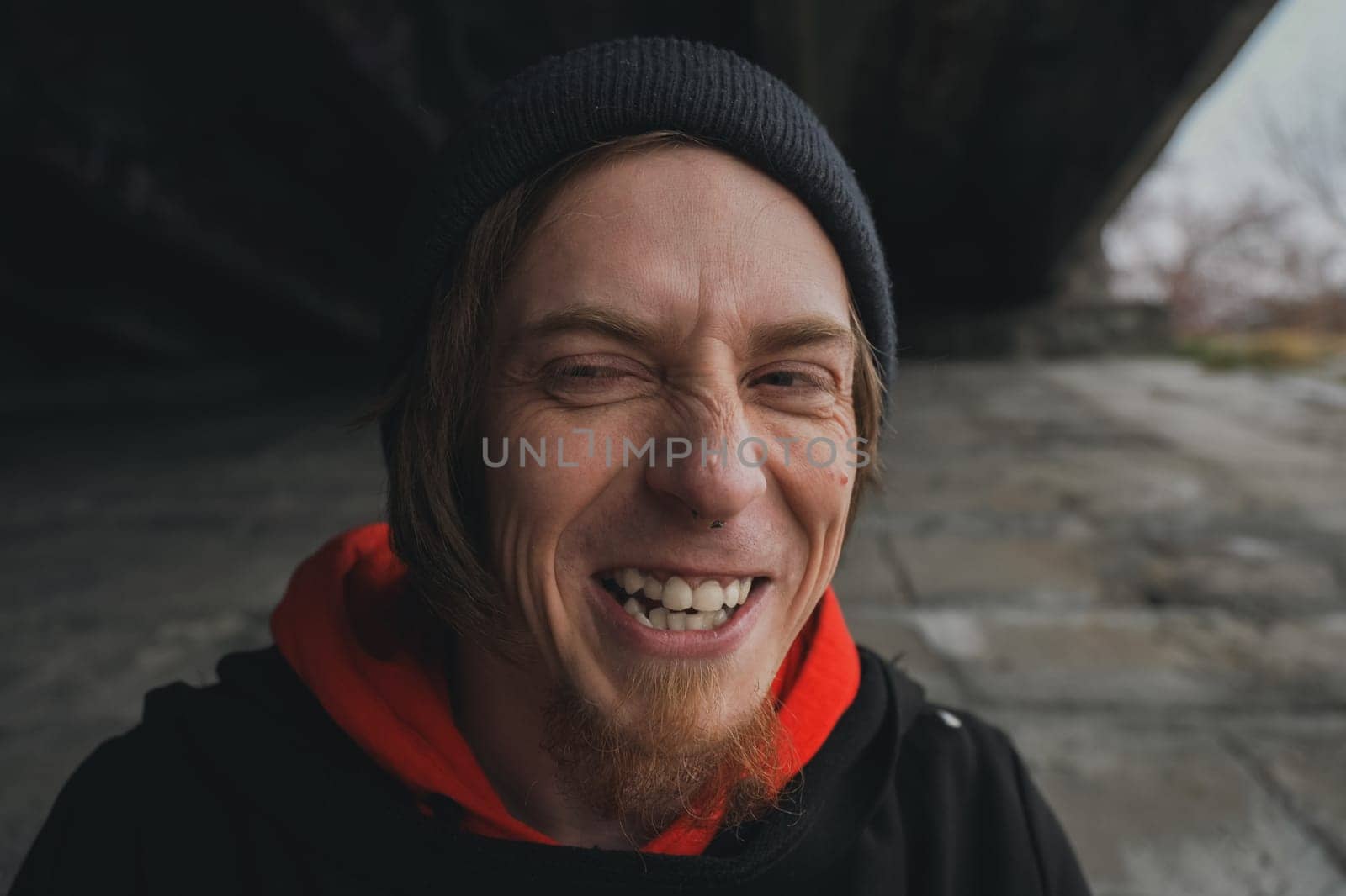 Beneath a towering bridge, a young man beams warmly, showcasing his vibrant spirit amidst the urban backdrop