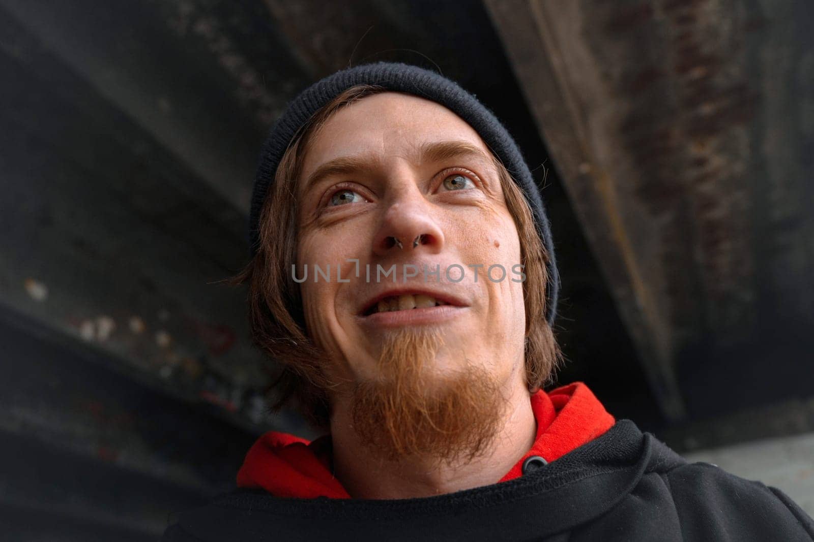 Beneath a towering bridge, a young man beams warmly, showcasing his vibrant spirit amidst the urban backdrop