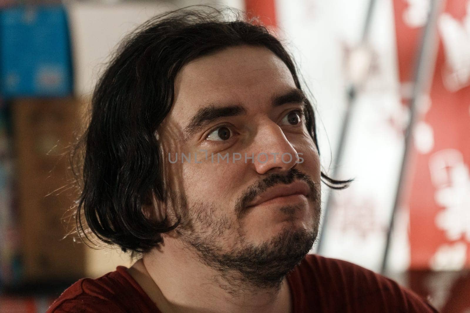 A man with a contemplative expression sits, surrounded by vibrant colors and lively atmosphere. Selective focus