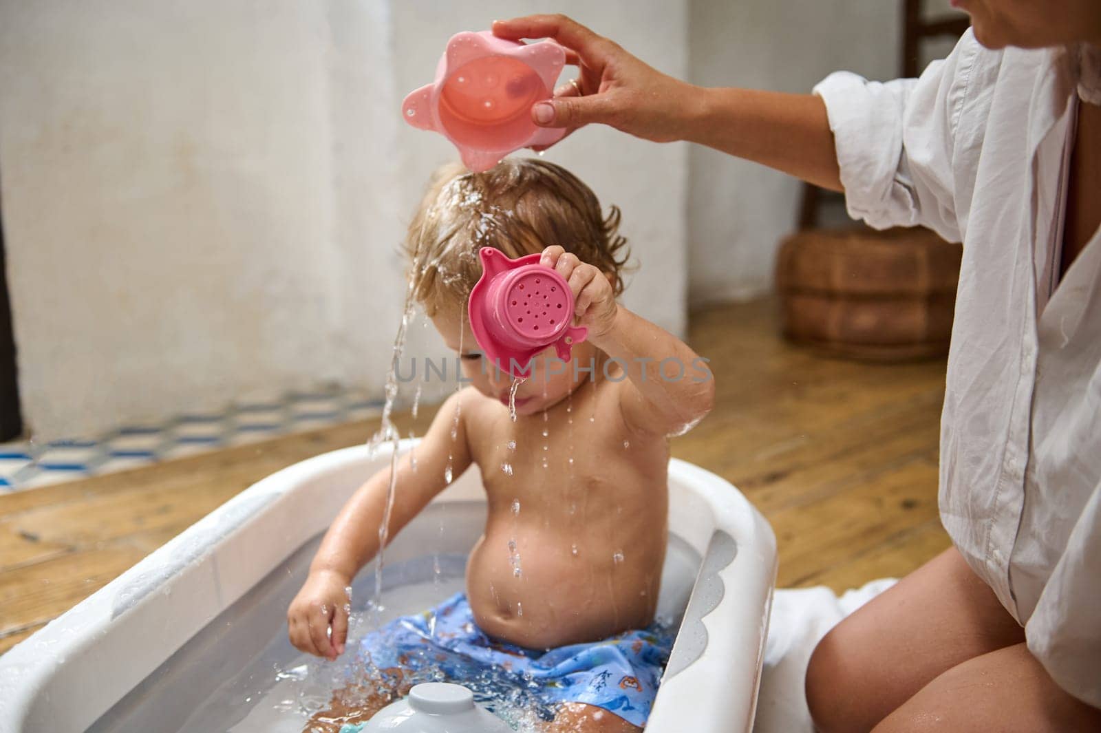 A toddler plays with water toys while being bathed by a parent in a cozy home environment. The playful and bonding moment highlights childhood joy and family care.