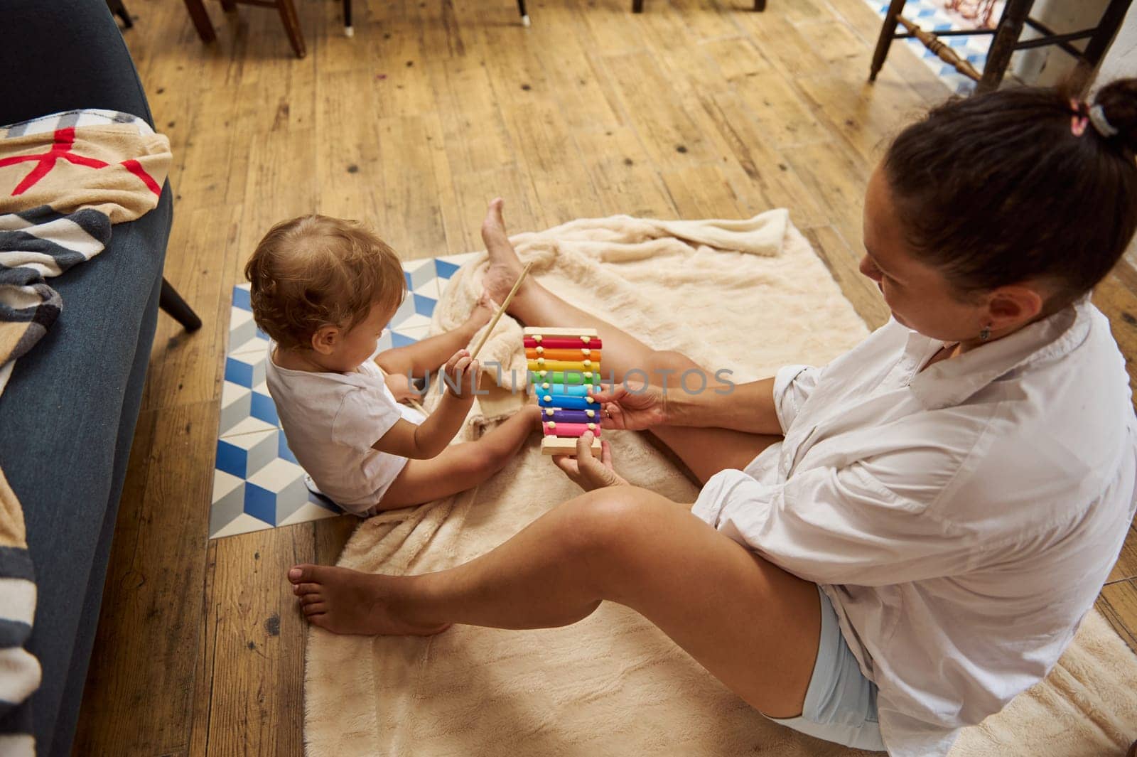 A mother and her baby engage in playful interaction using a colorful xylophone on a cozy floor setting, fostering early learning and bonding.