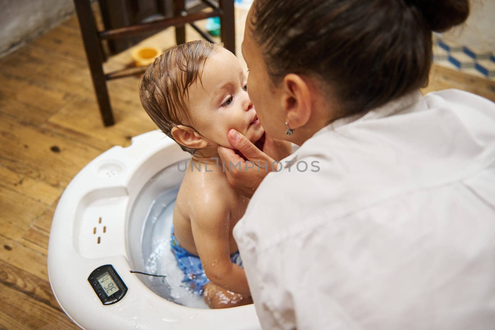 A mother lovingly bathes her baby in a white tub, showcasing tender care and family bonding in a cozy home setting.