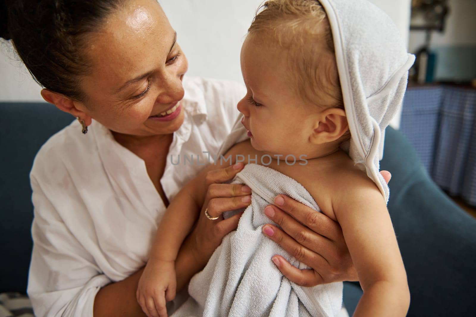 A tender moment between a mother and her infant after a bath. The baby is wrapped in a soft towel, sharing a loving gaze with the mother, creating a warm, nurturing atmosphere.