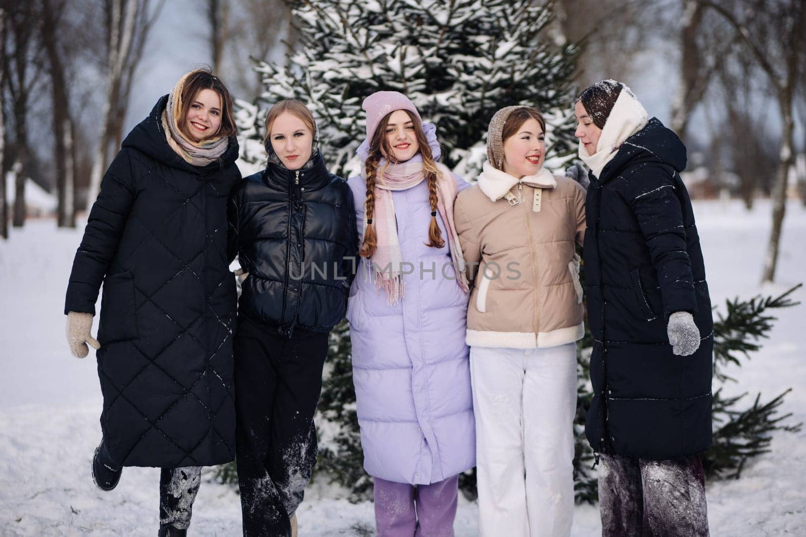 Five joyful schoolgirls, wrapped up in cozy winter coats, delight in a snowy day by a pine tree, celebrating their friendship and the beauty of the winter season