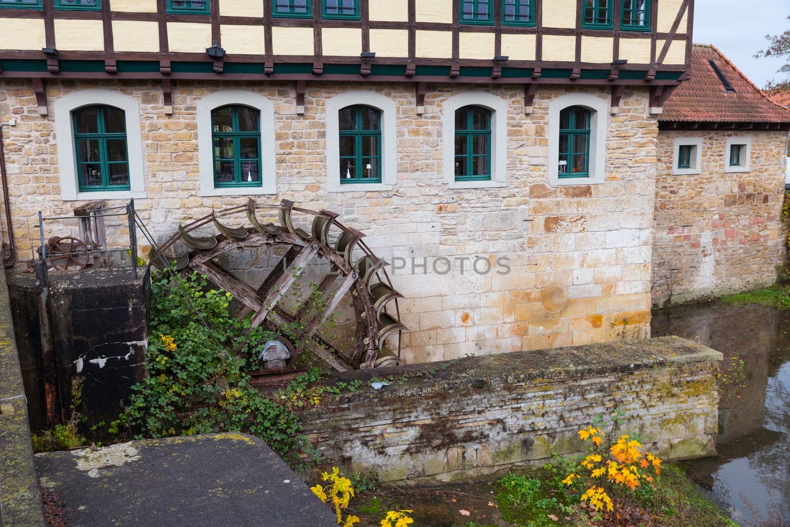a charming historic watermill adjacent to a stone building, surrounded by lush greenery and vibrant flowers, reflecting a serene and rustic atmosphere in steinfurt germany