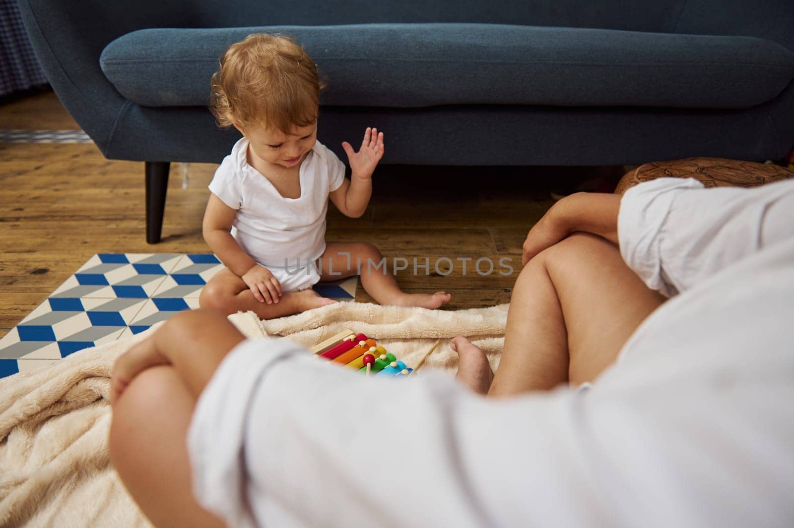 A baby plays joyfully with colorful toys on a soft blanket at home. Family bonds, cozy and playful atmosphere, and early childhood development are highlighted in this warm and intimate scene.