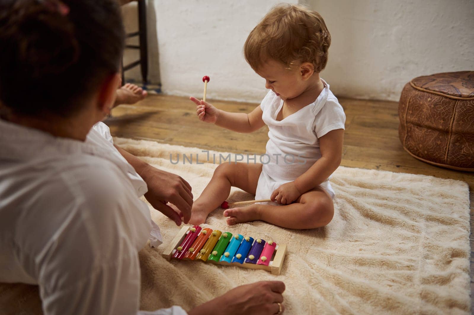 A mother and her toddler engage with a colorful xylophone on a soft carpet, encouraging learning and bonding through music in a cozy home setting.