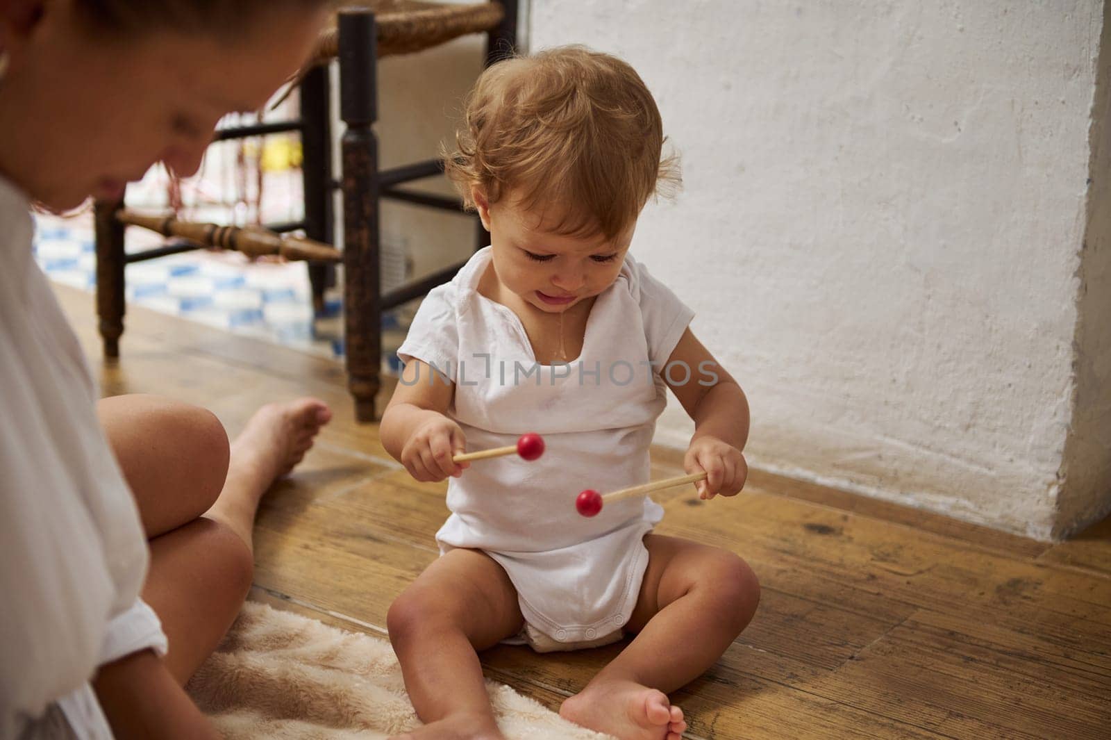 A young child is joyfully playing with wooden toys on the floor. The cozy setting suggests a warm family atmosphere, filled with playfulness and exploration.
