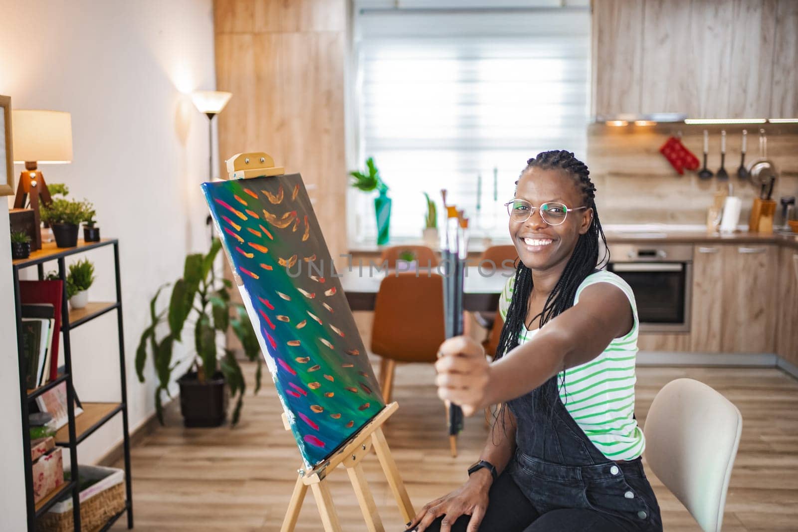 An artist smiles while holding a paintbrush in a stylish kitchen.
