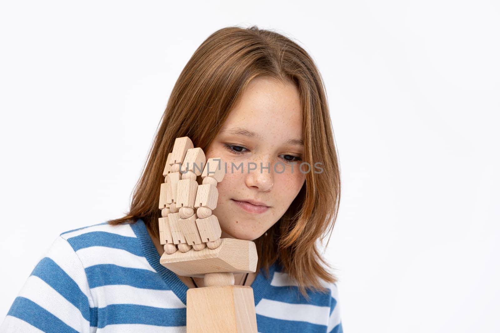 A young girl deeply ponders and contemplates while engaging with a wooden hand model in a minimalist studio setting