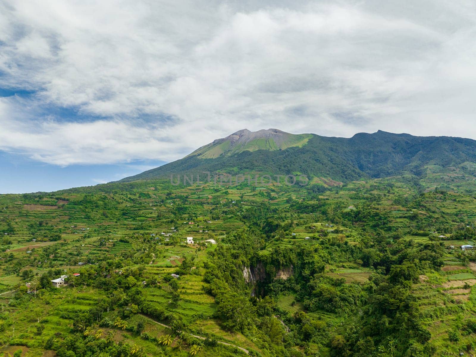 Aerial view of farmland with plantings against a background of mountains and blue sky. Kanlaon volcano. Negros, Philippines