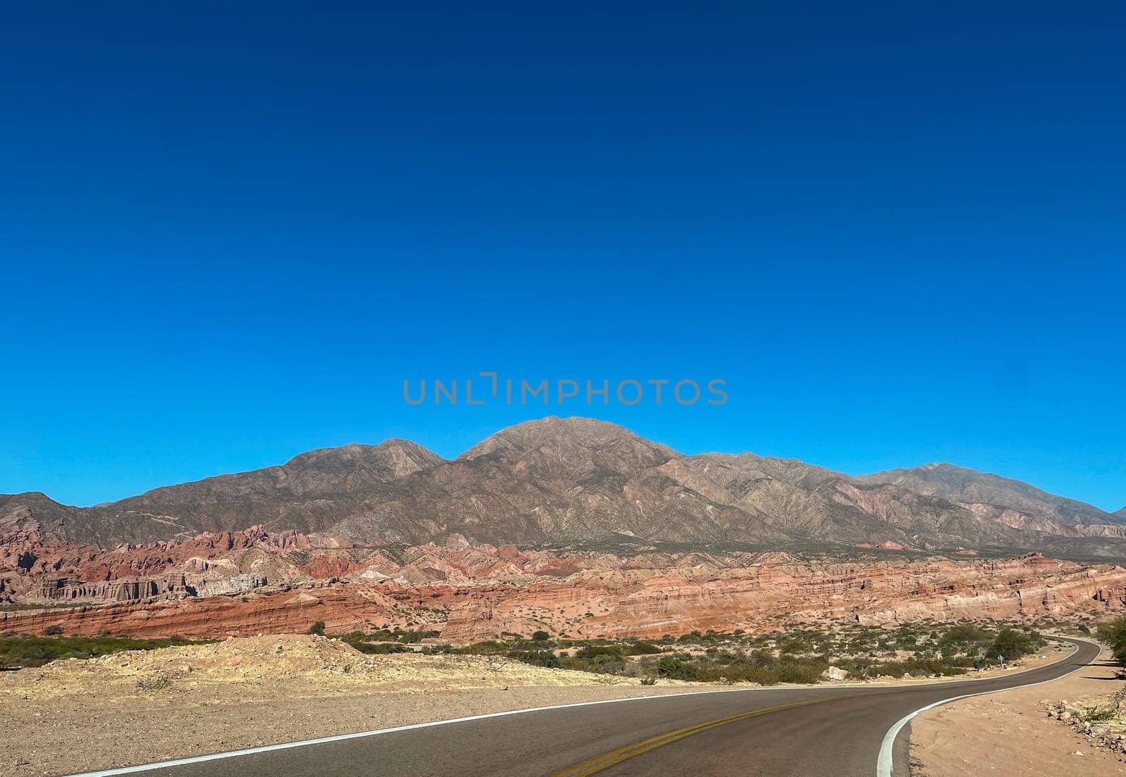Intricate road between colourful mountains in a sunny day. Adventure tourism. Winter holidays in Argentina. Wallpaper for tourism promotions