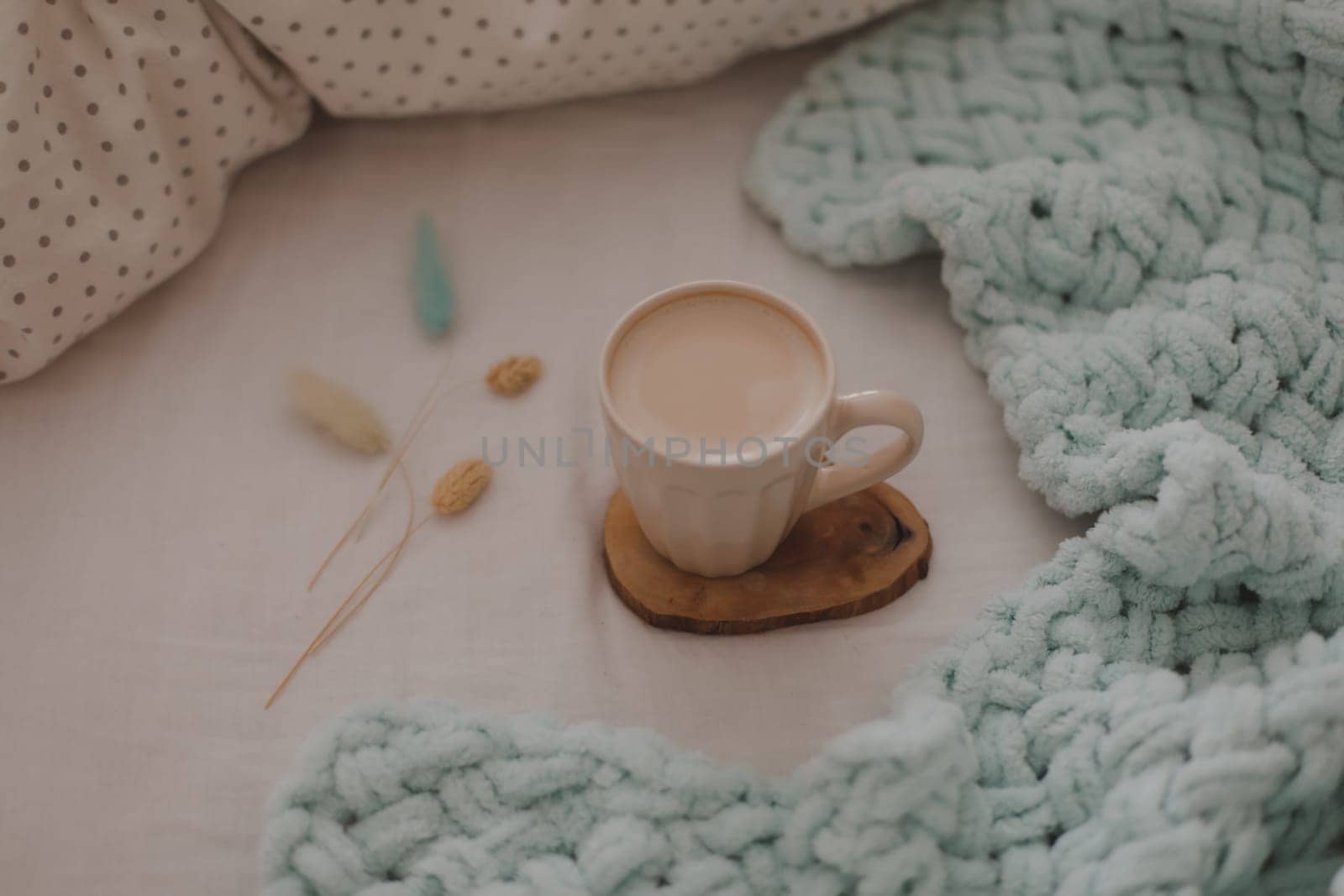 Cup of coffee with milk on the bed with white linens and blanket. Morning coffee in bed concept