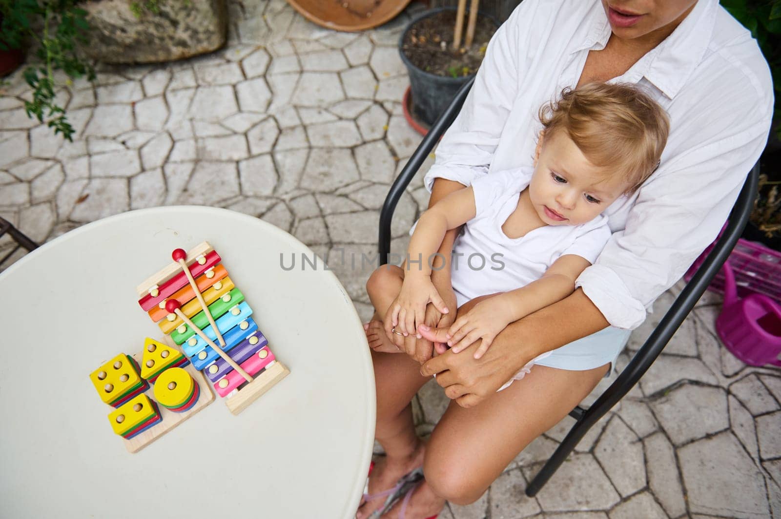 A mother and her young child enjoy playtime outdoors with vibrant toys on a table. The scene exudes warmth and nurturing, capturing a moment of family bonding and development.