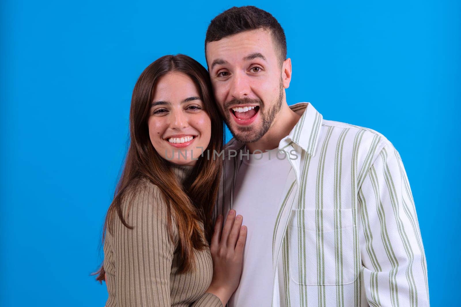 A joyful young couple embracing and smiling warmly at the camera against a vibrant blue background. Ideal image for love, relationships, happiness, or positive lifestyle concepts.