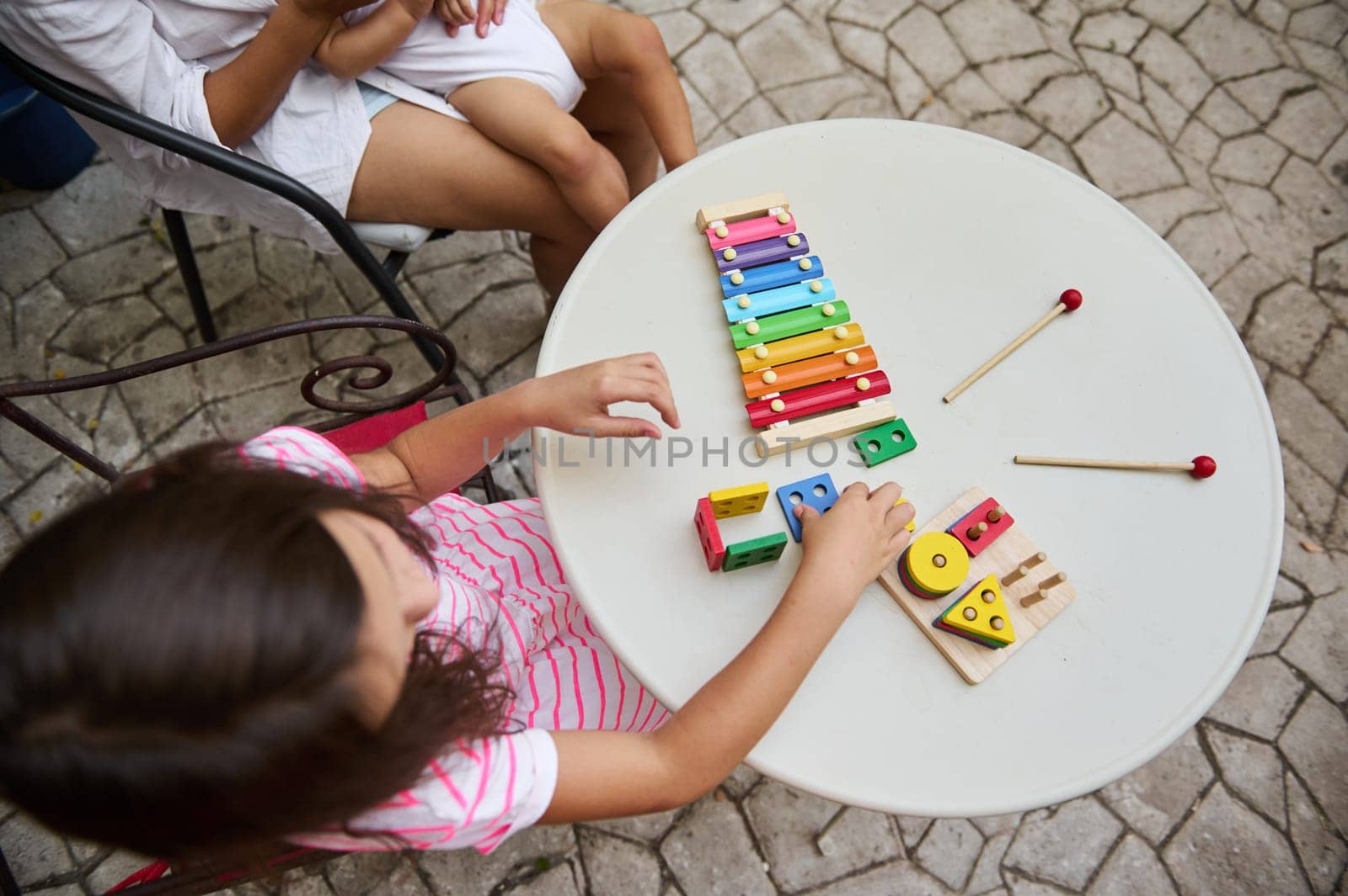A child engaged with a colorful xylophone and wooden blocks on an outdoor table, enjoying playful learning.