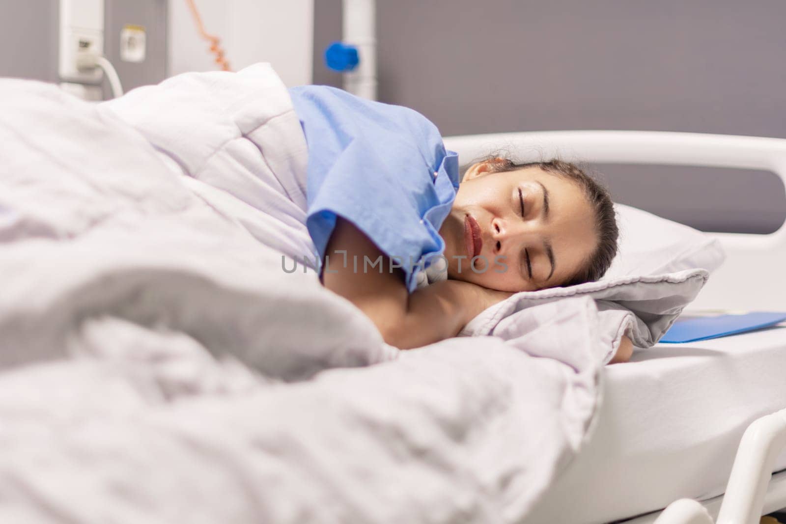 Young woman in blue robe lying comfortably and getting ready for bed on hospital bed in calm environment of clinic in private room, soft lighting, concept of recovery and care,