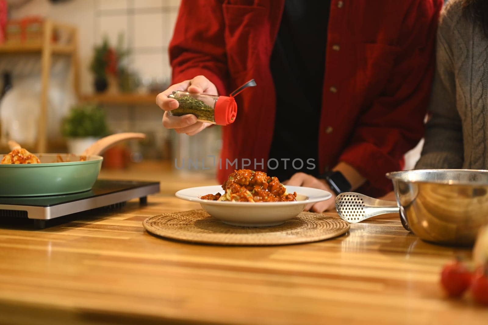 Close up of man garnishing a plate of freshly prepared pasta with dried herbs.