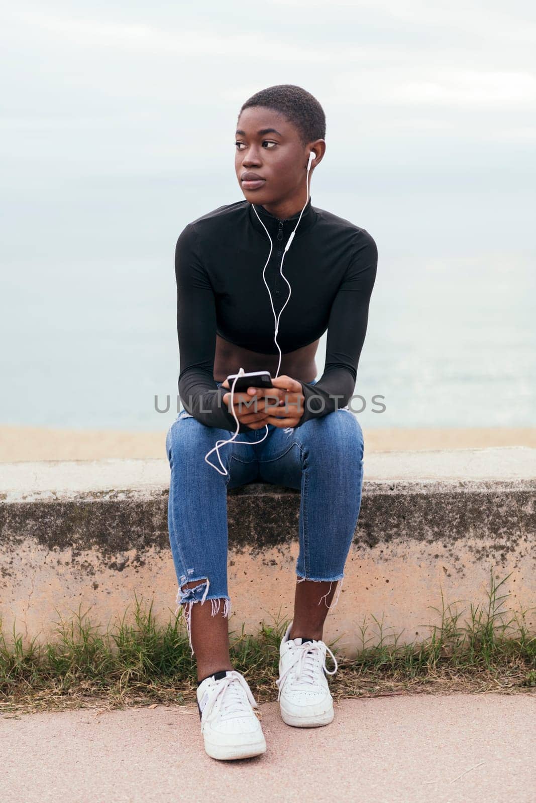 african american woman with short hair listening music with earphones on mobile phone, concept of youth and technology