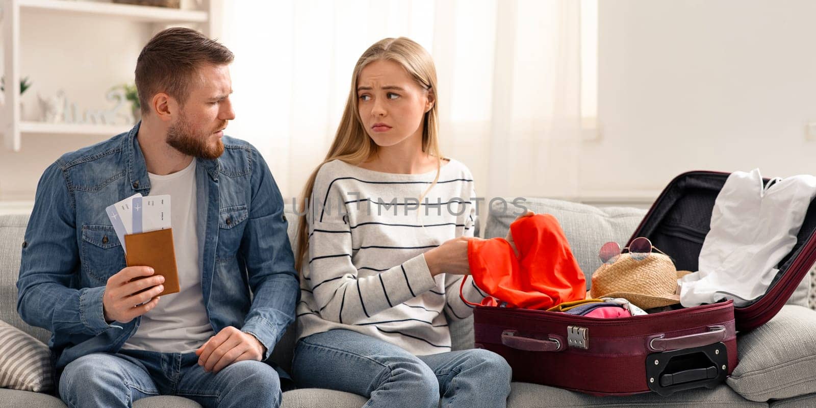 Vacation disaster. Sad couple suffering unpacking suitcase for trip at home, empty space