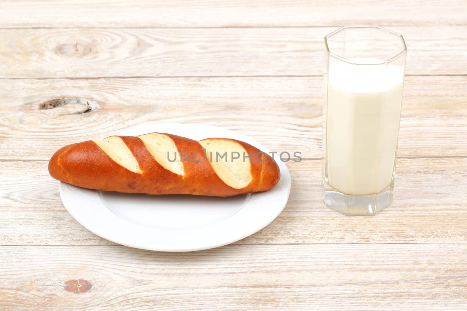 A perfectly freshly baked breadstick accompanied by a cold glass of milk on a rustic wooden dining table