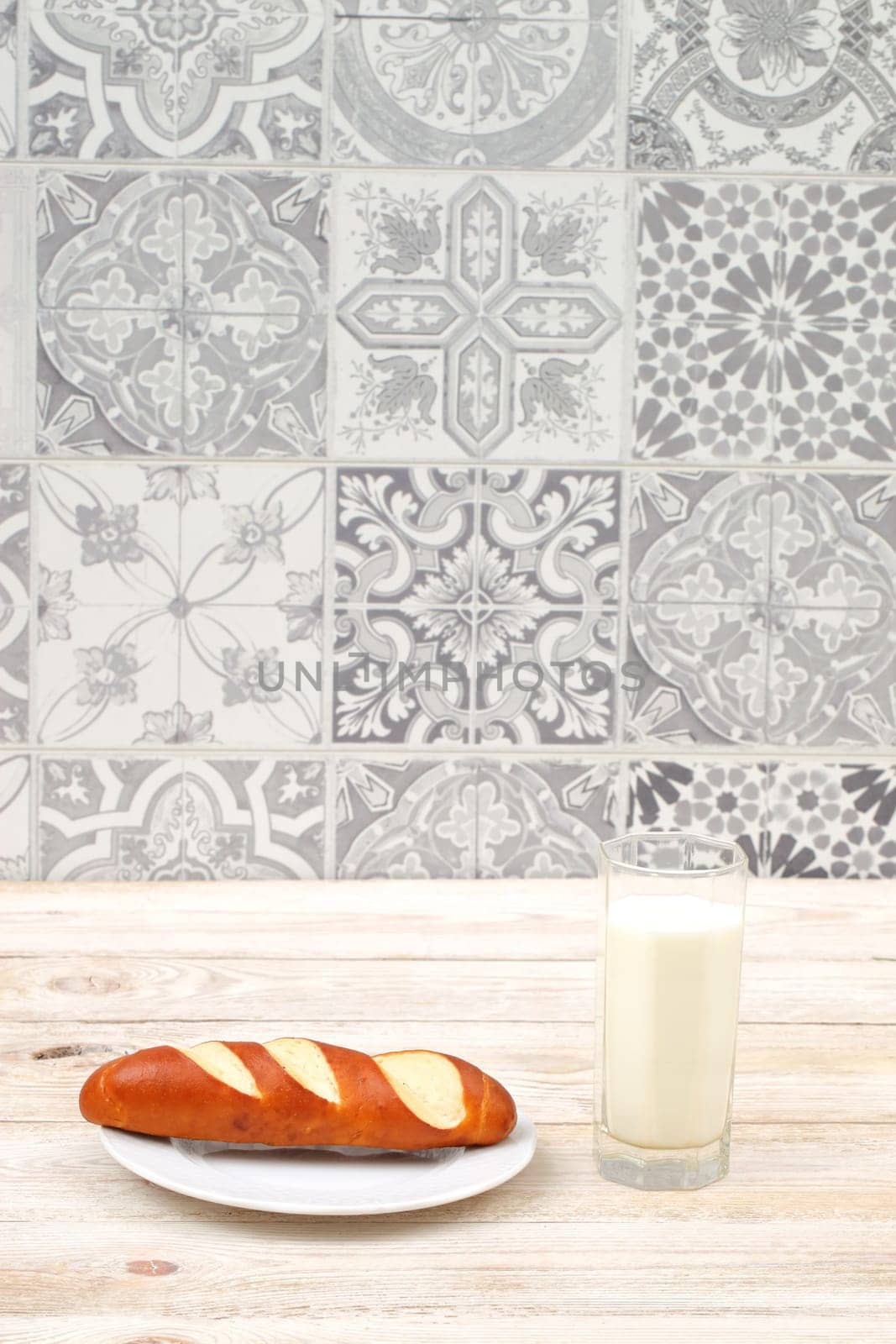 A rustic setting features freshly baked bread and a glass of milk, enhanced by a lovely tile background