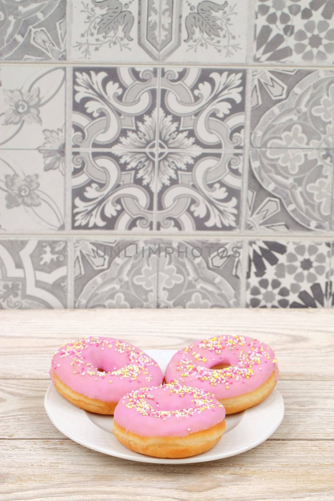 Three enticing pink donuts with colorful sprinkles, beautifully arranged against a decorative tile background