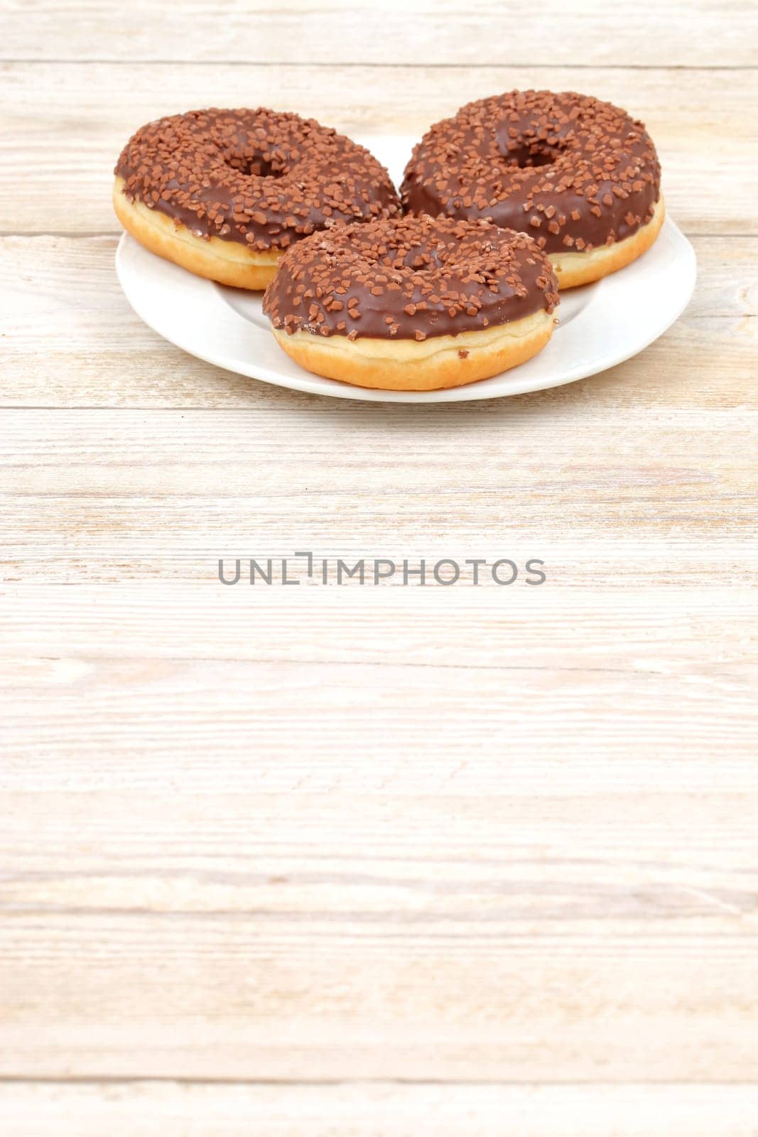Three mouthwatering chocolateglazed donuts adorned with colorful sprinkles resting on a rustic wooden table