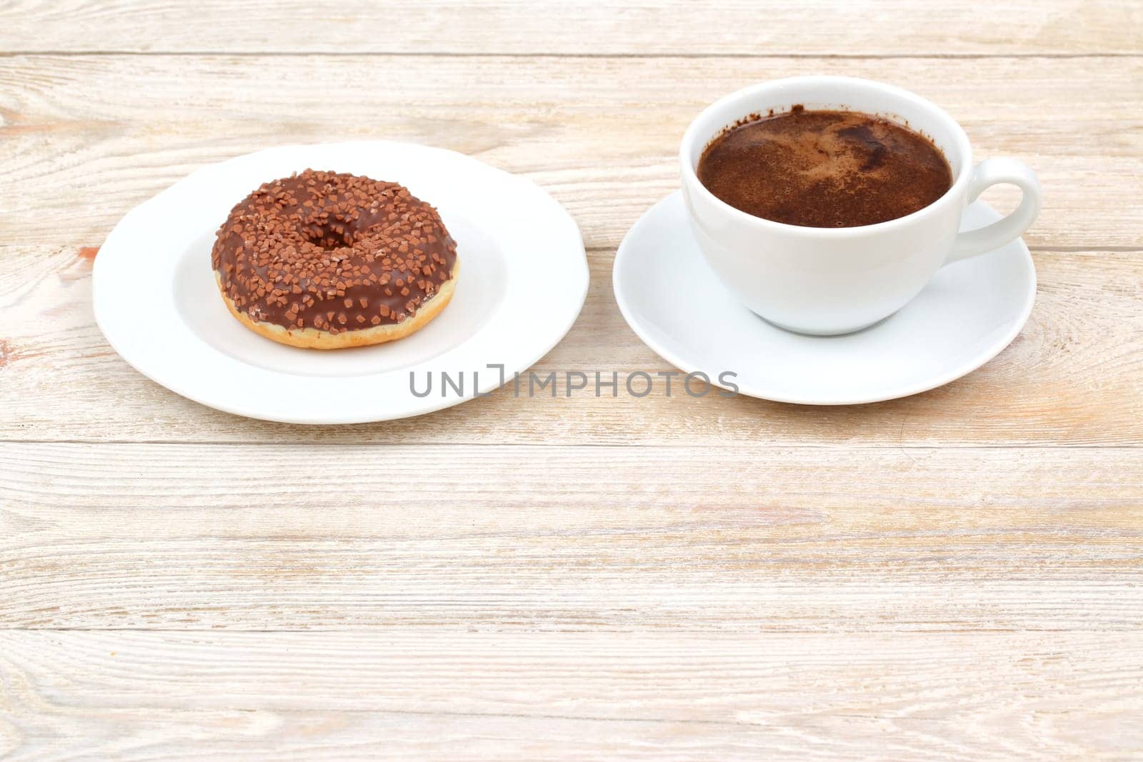 A delicious chocolate donut is served alongside a steaming hot cup of coffee on a charming rustic wooden table