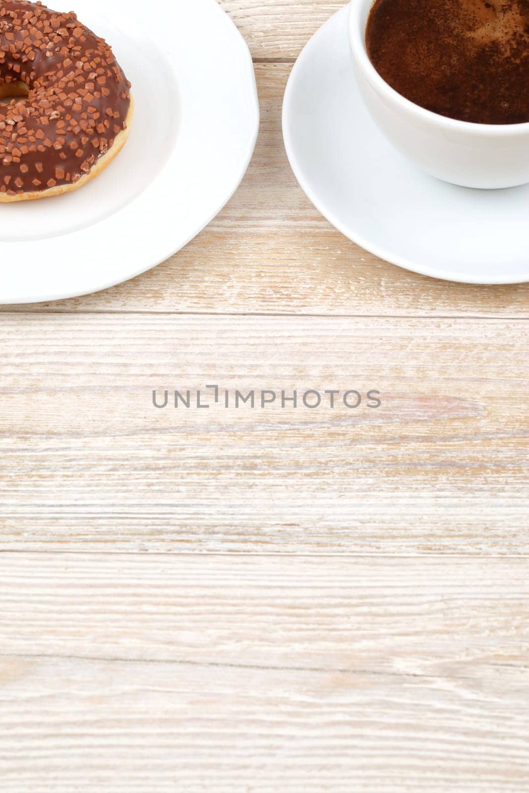 Enjoy a hot cup of coffee with a fresh chocolate donut, elegantly presented on a rustic wooden table