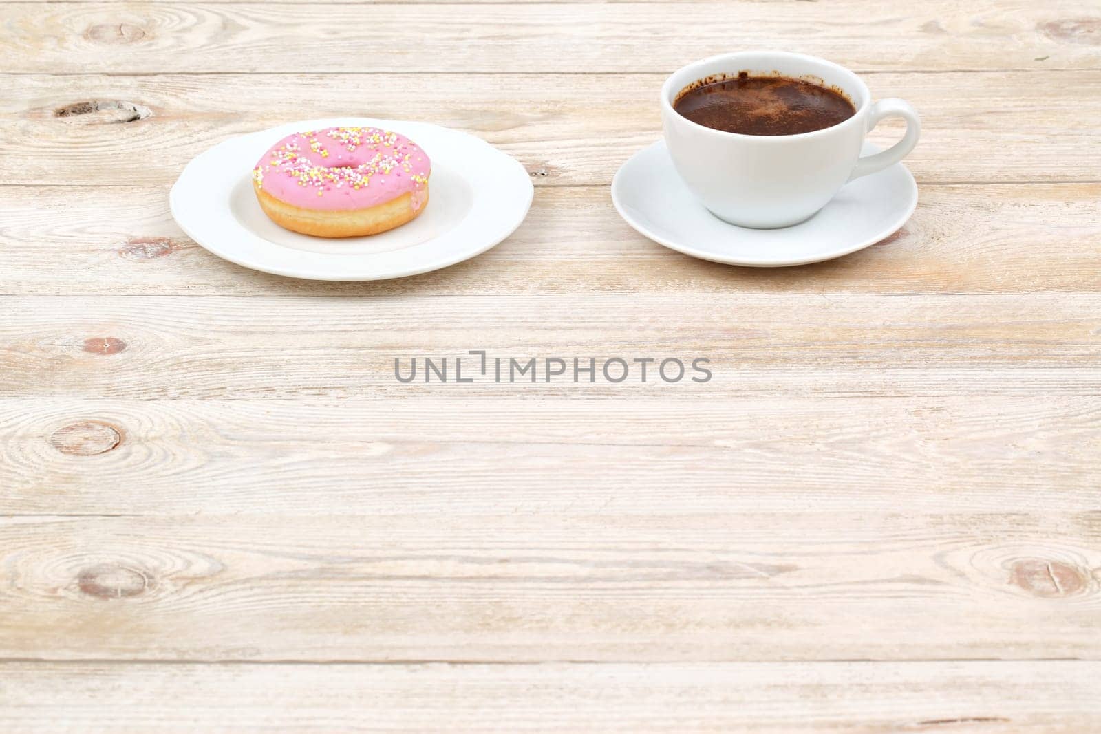 A delightful and charming coffee cup paired perfectly with a pink frosted donut, set on a rustic wooden table