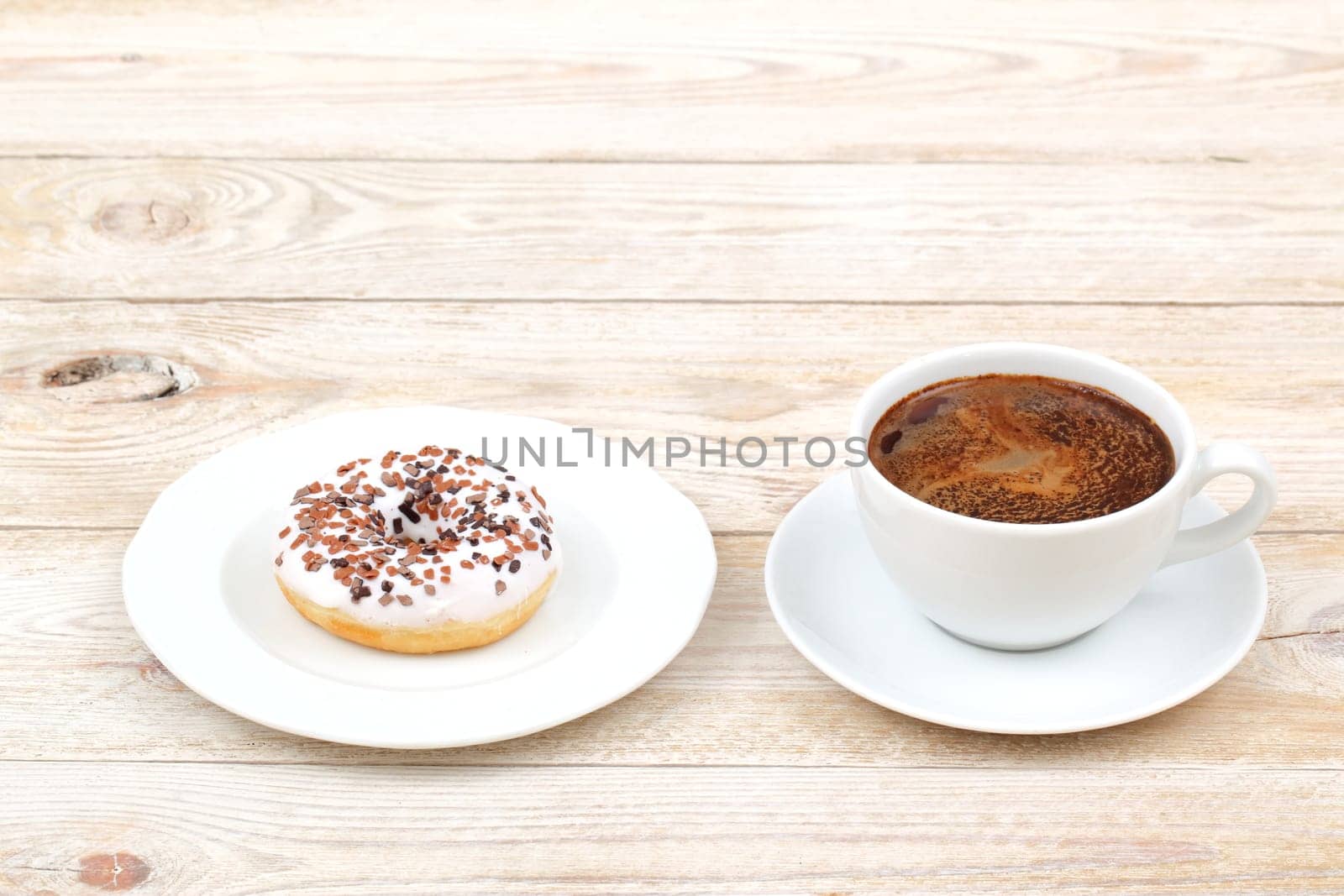 A delicious donut topped with chocolate sprinkles is sitting next to a steaming cup of coffee on a rustic wooden table