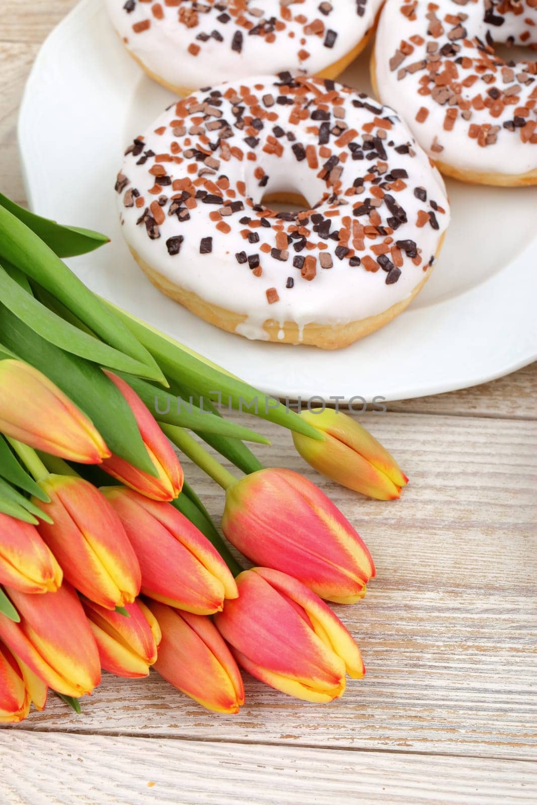 A delightful display of mouthwatering donuts with colorful sprinkles and vibrant tulips on a wooden surface