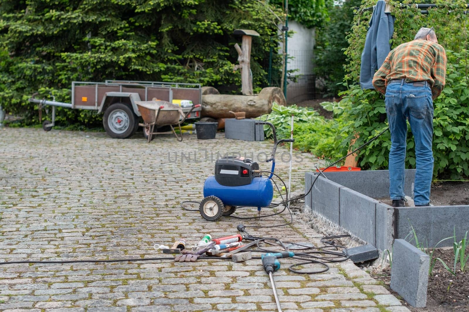Middle aged man using various tools to build a greenhouse in his garden, home eco vegetable growing concept,gardener stands inside a structure made of concrete slabs.