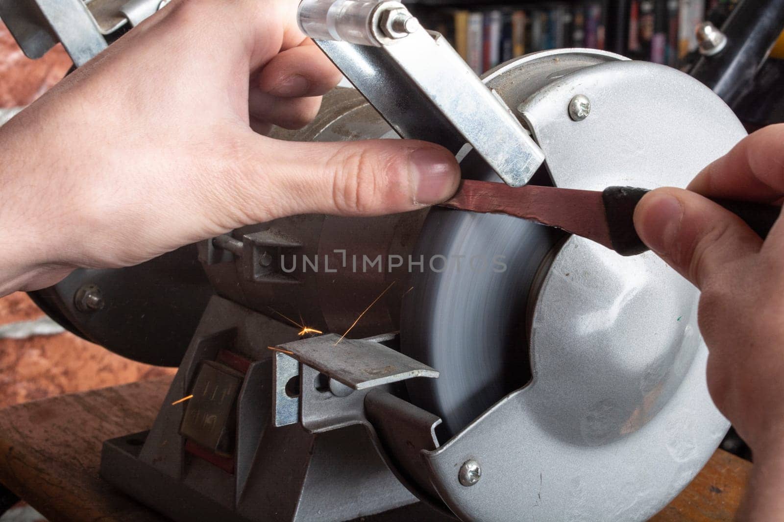 A knife sharpener and hand with a blade on a wooden table, close-up against a brick wall background