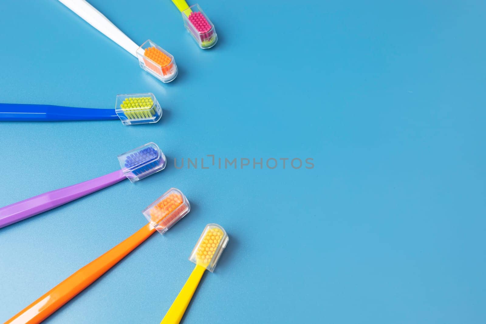 Flat Lay Few of Multicolored Toothbrushes Lying in Shape Of Sun On Blue Background, Space For Tex. Morning hygiene, Bathroom accessories. Dental Health Care. Horizontal Top View Plane by netatsi
