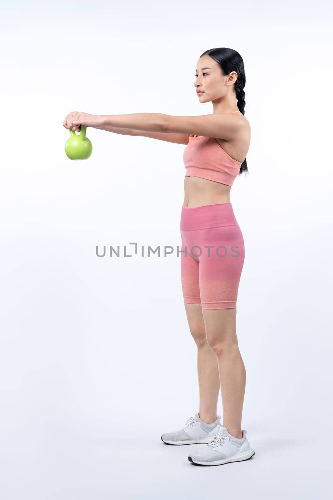 Vigorous energetic woman doing kettlebell weight lifting exercise on isolated background. Young athletic asian woman strength and endurance training session as body workout routine.