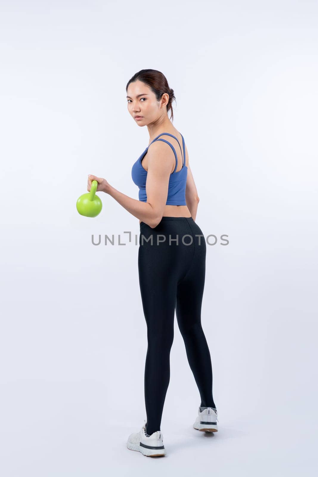 Vigorous energetic woman doing kettlebell weight lifting exercise on isolated background. Young athletic asian woman strength and endurance training session as body workout routine.