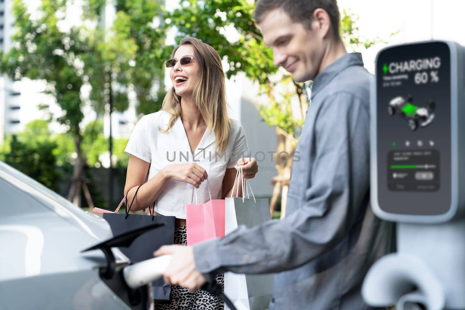 Young couple travel with EV electric car charging in green sustainable city outdoor garden in summer shows urban sustainability lifestyle by green clean rechargeable energy of electric vehicle innards