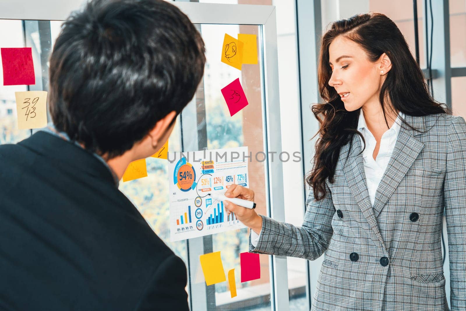 Business people work on project planning board in office and having conversation with coworker friend to analyze project development . They use sticky notes posted on glass to make it organized. Jivy