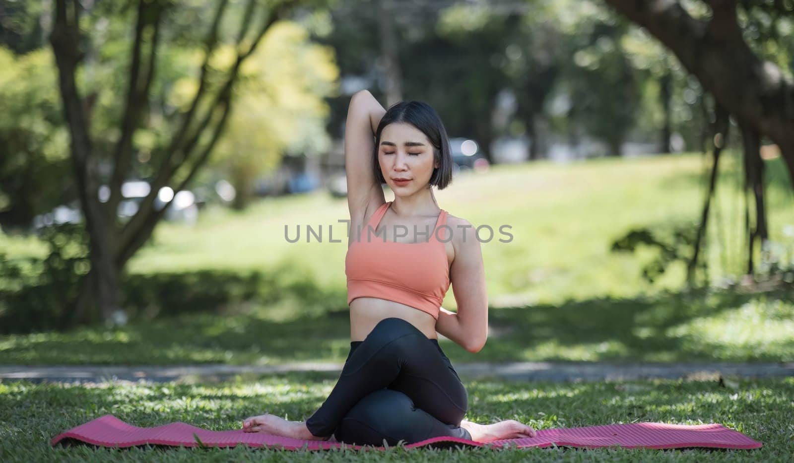 Attractive and charming Asian woman in her 30s in sportswear doing yoga poses, relaxing muscles. Asian woman practicing yoga in a beautiful green park by wichayada