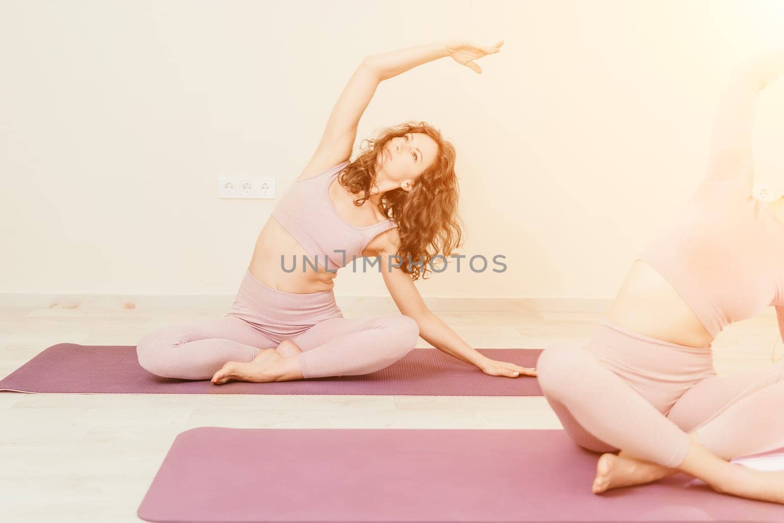 Well looking middle aged sporty woman, fitness instructor in pink sportswear doing stretching and pilates on yoga mat in the studio with mirror. Female fitness yoga. Healthy lifestyle and harmony. by panophotograph