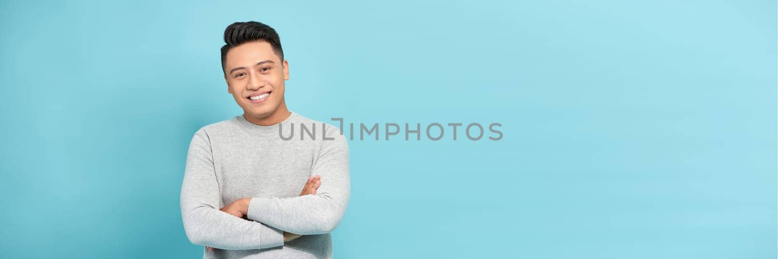 Attractive young smart Asian man crossing arms isolated on blue banner background. by makidotvn