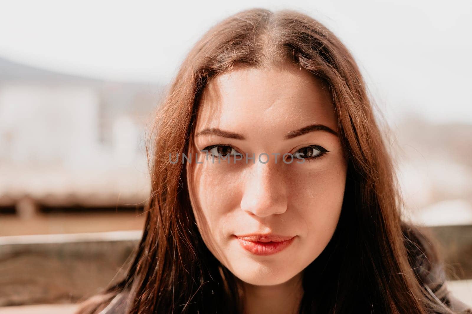 Happy young smiling woman with freckles outdoors portrait. Soft sunny colors. Outdoor close-up portrait of a young brunette woman and looking to the camera, posing against nature background.