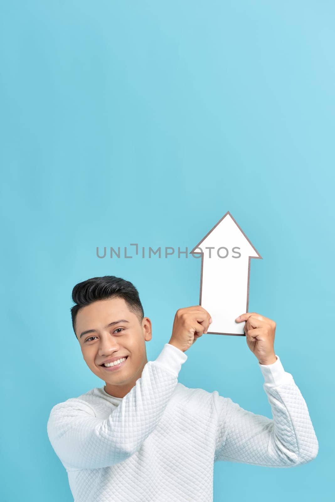 Smiling man holding white arrow isolated on a blue background