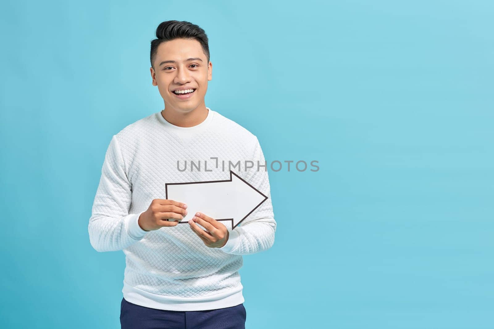 Good looking young man holding a white arrow, isolated on a blue background