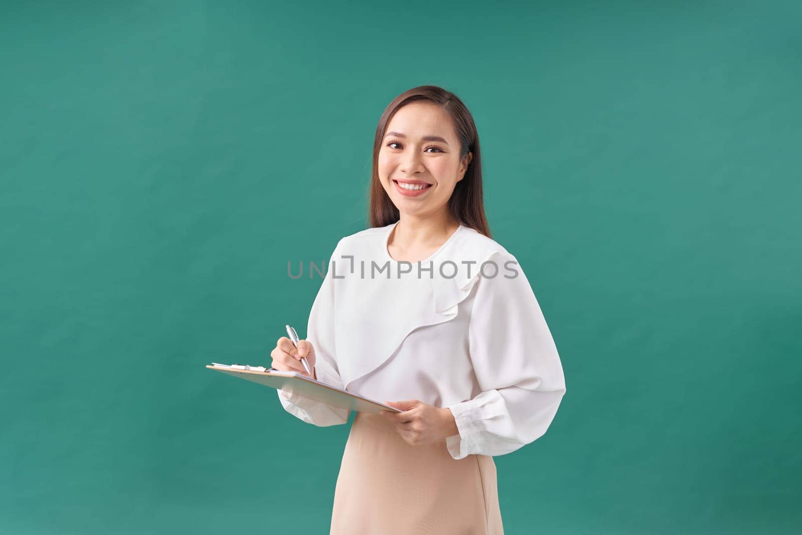 Beautiful business woman taking notes on her clipboard isolated on green background