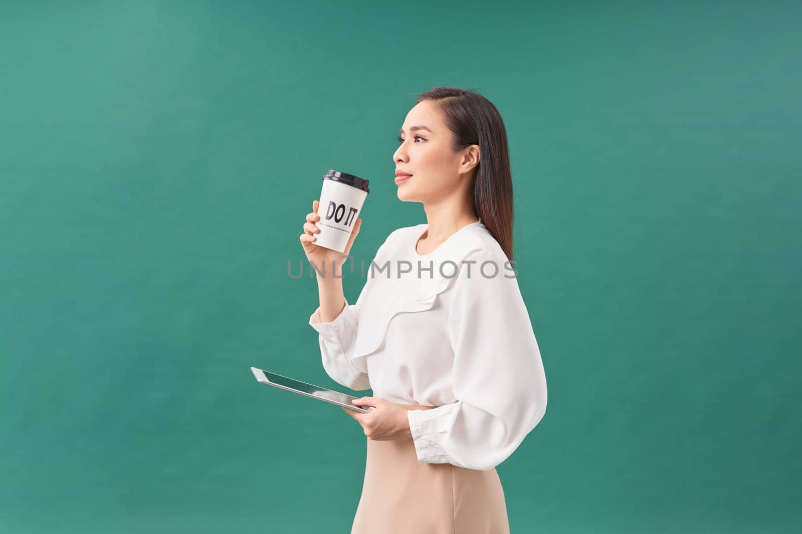 young woman holding digital tablet and paper cup isolated on green