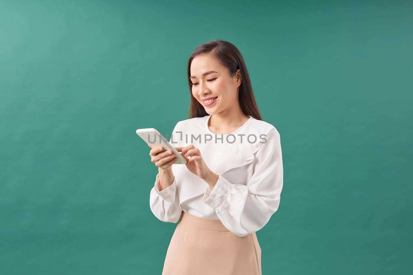 Portrait of a smiling casual woman holding smartphone over green background